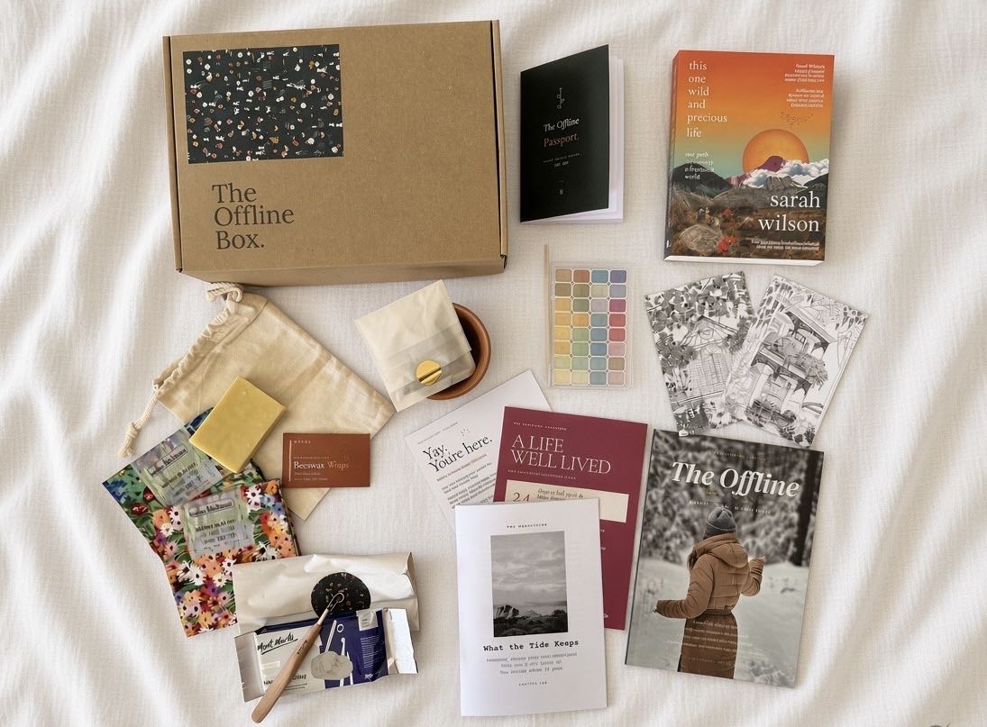 An Offline Box laid out on a timber table: a novel, the magazine, a spoon, seeds and the sealed Manuscript